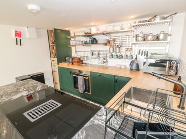 A kitchen with green cabinets a stovetop a wooden countertop shelves with dishes and cookware and a sink at 16 Arwenack Street in Falmouth