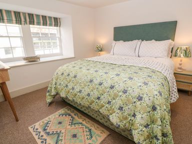 A bedroom with a double bed featuring patterned bedding two bedside lamps a window with striped curtains and a small rug on the floor at 16 Arwenack Street in Falmouth