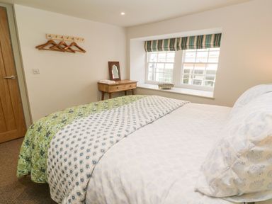 A bedroom with a bed a wooden desk with a mirror a window with striped blinds and a wall coat rack at 16 Arwenack Street in Falmouth