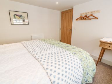 A bedroom with a bed covered with patterned bed covers a wooden door a wall-mounted coat rack with hangers a small wooden side table with towels and a framed artwork on the wall at 16 Arwenack Street in Falmouth
