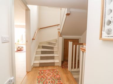 A hallway with stairs carpeted in the middle and wooden handrails a doorway leading to a bright room and a framed shell artwork on the wall at 16 Arwenack Street in Falmouth