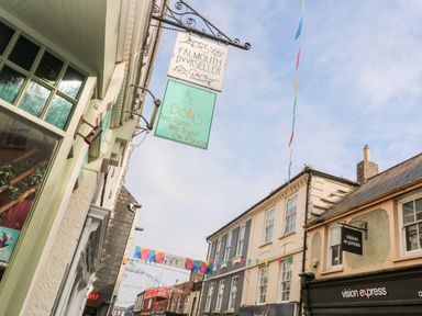 Street view with hanging signs for Falmouth Bookseller Dolly's Tea Room and Vision Express at 16 Arwenack Street in Falmouth
