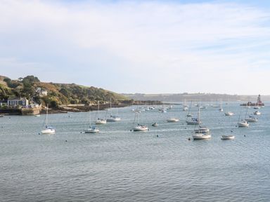 A coastal view with multiple sailboats anchored in the water near a shoreline with greenery and houses at 16 Arwenack Street in Falmouth