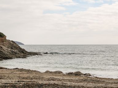 A rocky beach with seaweed and tire tracks visible at the shore with ocean waves and cloudy sky at 16 Arwenack Street in Falmouth