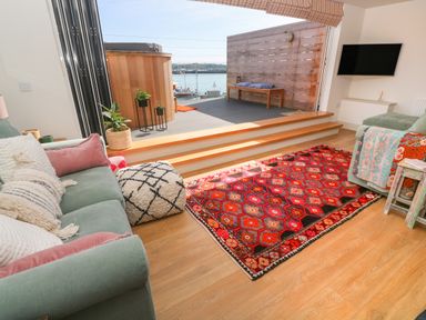 A living room with green sofas and a red patterned rug leading to a deck with a wooden bench and hot tub at 16 Arwenack Street in Falmouth