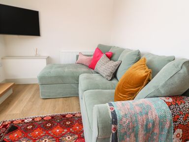 A living room with a sectional sofa with cushions a patterned throw and a wall-mounted television at 16 Arwenack Street in Falmouth