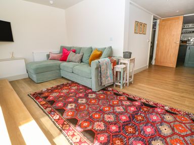 A living room with a green sectional sofa with colorful cushions and a patterned rug at 16 Arwenack Street in Falmouth