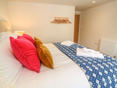 A bedroom with a bed with colorful pillows and folded towels on a blue patterned runner at 16 Arwenack Street in Falmouth