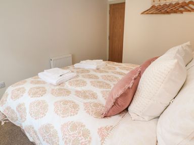 A bedroom with a bed covered in patterned bedding with two folded towels on top and wooden hangers on the wall at 16 Arwenack Street in Falmouth