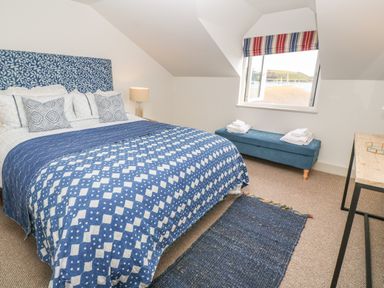 A bedroom with a blue patterned bedspread a blue bench with towels under a window and a wooden desk at 16 Arwenack Street in Falmouth