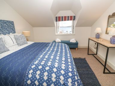 A bedroom with a bed covered with blue and white patterned bedding a bench under a window with a view of boats and a wooden desk with two lamps and a mirror at 16 Arwenack Street in Falmouth