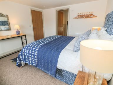 A bedroom with a bed covered with blue and white bedding a wooden desk with a blue lamp a mirror and wooden doors at 16 Arwenack Street in Falmouth