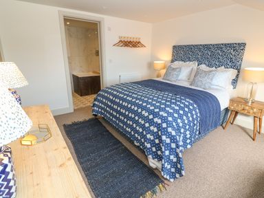 A bedroom with a patterned blue bedspread lamps on wooden tables and an open door to a bathroom at 16 Arwenack Street in Falmouth