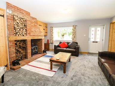 A living room with two brown leather sofas a wooden coffee table a brick fireplace and a window at Keepers Cottage in Beeston near Dereham