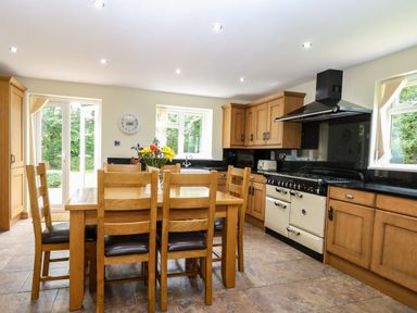 A kitchen with wooden cabinets a dining table with six chairs and flowers on the table at Keepers Cottage Beeston near Dereham