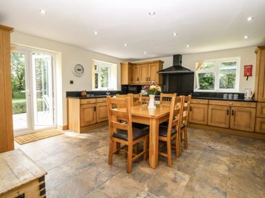 A kitchen with wooden cabinets a dining table with chairs and flowers by glass doors at Keepers Cottage in Beeston near Dereham