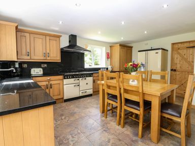 A kitchen with wooden cabinets black countertops a dining table with chairs and a vase of flowers at Keepers Cottage Beeston near Dereham