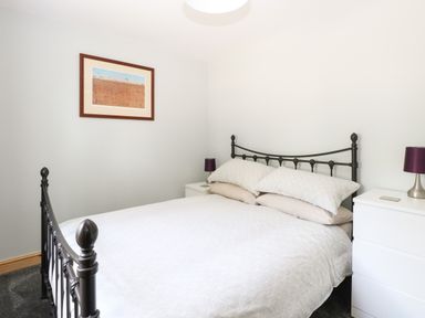 A bedroom with a metal bed frame white bedding two bedside tables with purple lamps and a framed picture on the wall at Keepers Cottage in Beeston near Dereham