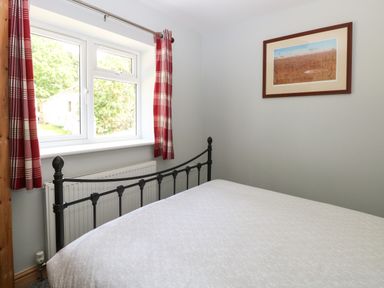 A bedroom with a metal bed frame white bedspread red check curtains a window and framed artwork on the wall at Keepers Cottage in Beeston near Dereham