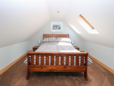A bedroom with a wooden bed frame striped bedding two bedside tables with lamps and skylight windows at Keepers Cottage in Beeston near Dereham