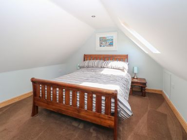 A bedroom with a wooden bed and striped bedding under a sloped ceiling with a skylight at Keepers Cottage in Beeston near Dereham