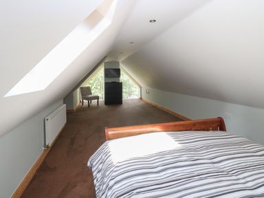 A bedroom with a striped bedspread a chair a chest of drawers and a television at Keepers Cottage in Beeston near Dereham