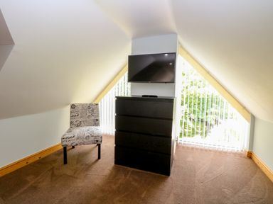 A room with a patterned chair a black chest of drawers and a wall-mounted television at Keepers Cottage in Beeston near Dereham