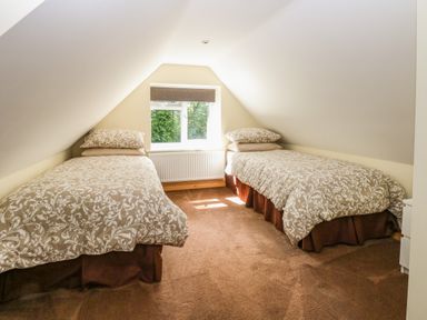 A bedroom with two single beds under sloped ceilings and a window between them at Keepers Cottage in Beeston near Dereham