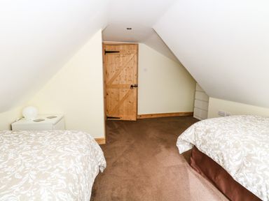 A bedroom with two beds white bedside table with lamp and wooden door at Keepers Cottage in Beeston near Dereham