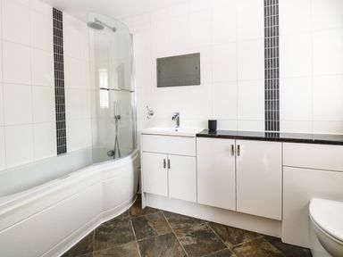 A bathroom with a bathtub shower combo, a sink with cabinetry, a mirror, and tiled walls at Keepers Cottage in Beeston near Dereham