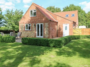 A brick house with patio furniture in a garden with grass and hedges at Keepers Cottage in Beeston near Dereham