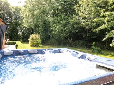 A garden with a bubbling hot tub and surrounding trees at Keepers Cottage in Beeston near Dereham