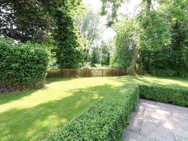 A garden with a stone patio hedge and wooden fence with trees at Keepers Cottage in Beeston near Dereham