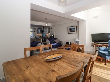 A dining area with a wooden table and chairs adjacent to a living room with sofas a TV and a blue armchair at Ferriwais in Appledore