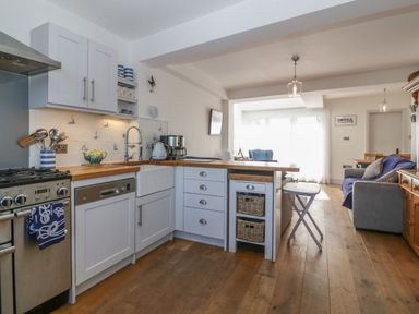 A kitchen with white cabinets and wooden countertops open to a living area with a sofa and dining table at Ferriwais in Appledore