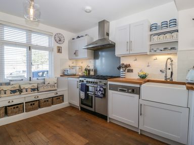 A kitchen with a window seat cushion and baskets a stove a dishwasher a sink and cupboards at Ferriwais in Appledore