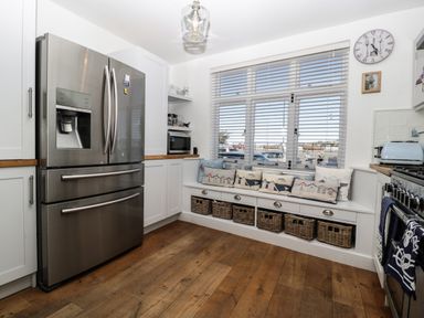 A kitchen with a stainless steel refrigerator, a window seat with cushions and wicker baskets underneath, a microwave, and a stove with towels at Ferriwais in Appledore
