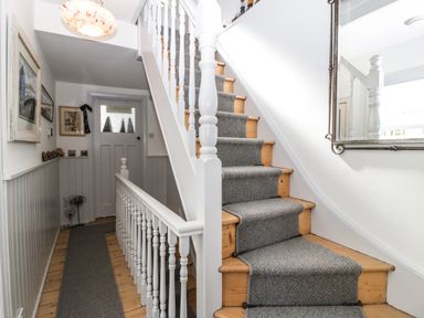 A hallway with wooden stairs covered by a gray carpet runner and a large mirror on the wall at Ferriwais in Appledore