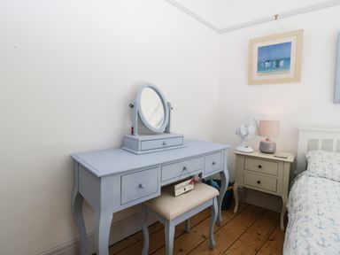 A bedroom corner with a blue dressing table and stool next to a bedside table with a fan and lamp at Ferriwais in Appledore