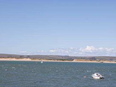 A boat floating on water near a sandy shoreline with hills in the background at Ferriwais Appledore