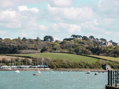 A coastal scene with boats on water and a hillside with trees and a building in the background at Ferriwais in Appledore