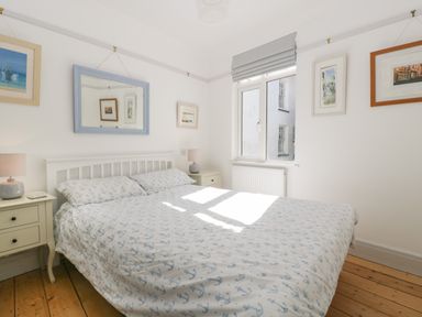 A bedroom with a bed with anchor patterned bedding two bedside tables with lamps a window and framed pictures at Ferriwais in Appledore