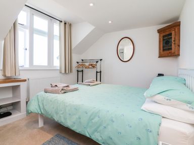 A bedroom with a bed with green bedding near a window with beige curtains and a wall mirror at Ferriwais in Appledore