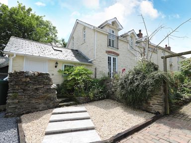 Exterior view of a two story stone house with a gravel path and garden with plants and bushes at Spring Cottage in Pentre Cwrt