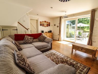 A living room with a corner sofa and a wooden coffee table next to sliding glass doors at Spring Cottage in Pentre-Cwrt