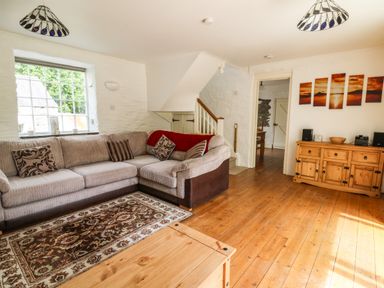 A living room with a sectional sofa a wooden cabinet and a staircase at Spring Cottage in Pentre-Cwrt