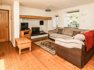 A living room with a sofa a coffee table a TV on a stand a wood stove and wooden flooring at Spring Cottage in Pentre-Cwrt