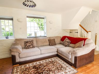 A living room with a sectional sofa pillows a red throw and a patterned rug at Spring Cottage in Pentre-Cwrt