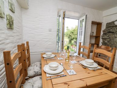 A dining room with a wooden table set for four with open double doors leading to a garden at Spring Cottage in Pentre-Cwrt