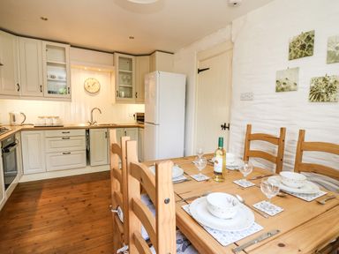 A kitchen with wooden dining table set for four and white cabinets at Spring Cottage in Pentre-Cwrt